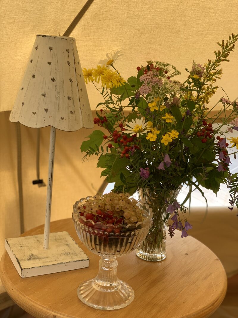 Glamping teltan sisällä oleva pöytä jossa on kukkakimppu, lamppu ja kulho