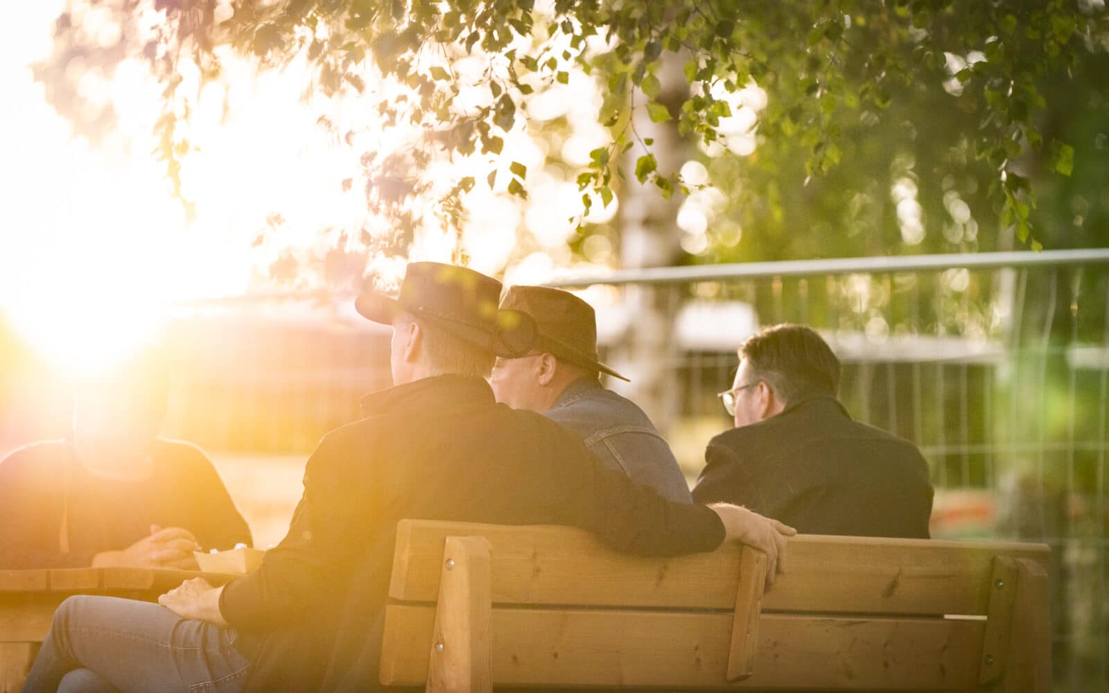 Kaksi miestä stetson-hatut päässä, ulkona penkillä, aurinkoisessa kesäillassa.