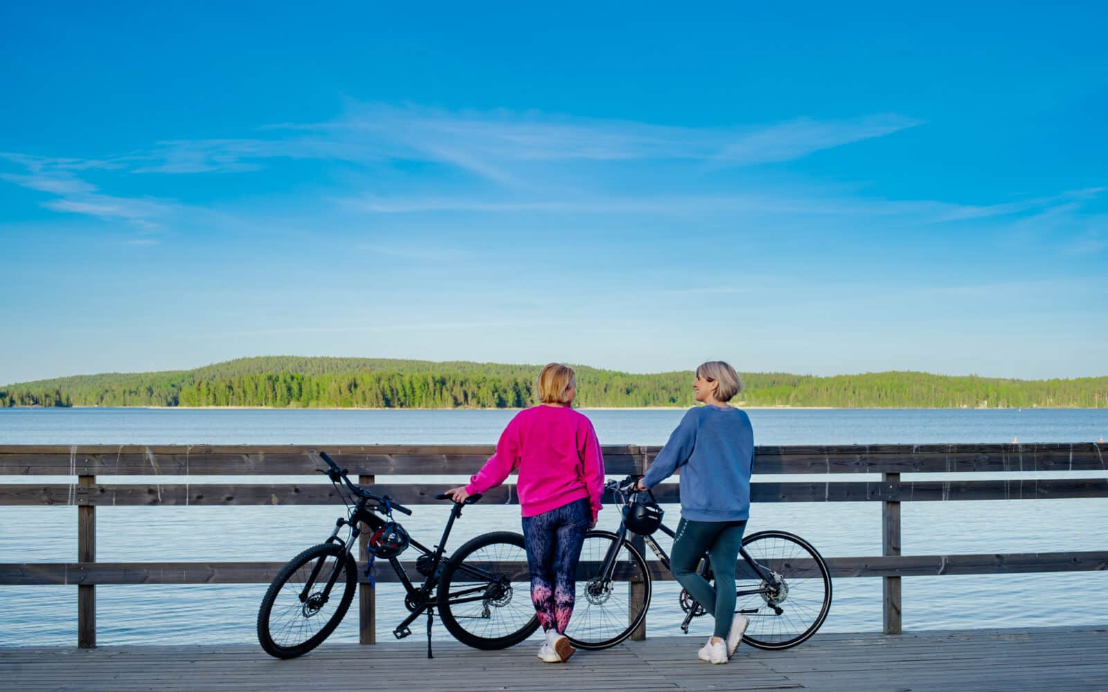 Kaksi naista pyörien kanssa järven rannalla